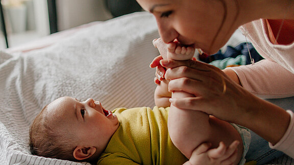Mutter spielt mit Baby auf Bett und hält Babyfüße