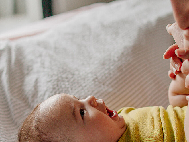 Mutter spielt mit Baby auf Bett und hält Babyfüße