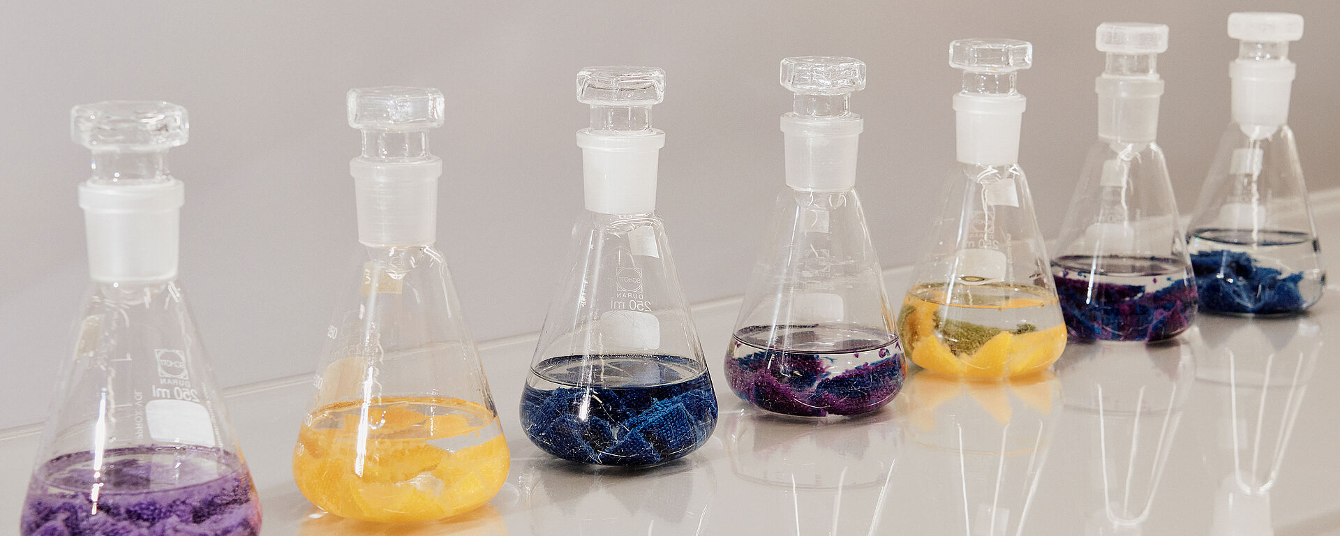 Glass laboratory flasks containing coloured textile pieces