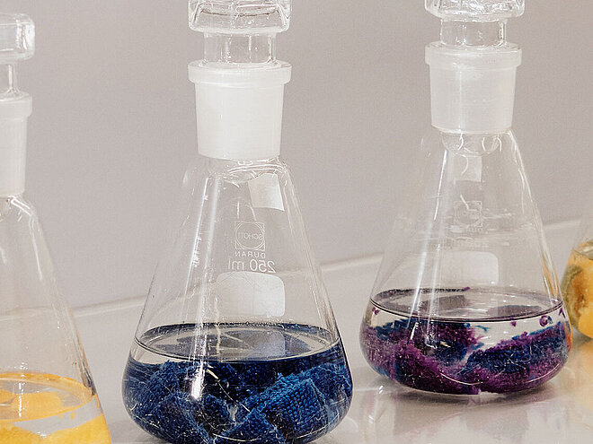 Glass laboratory flasks containing coloured textile pieces