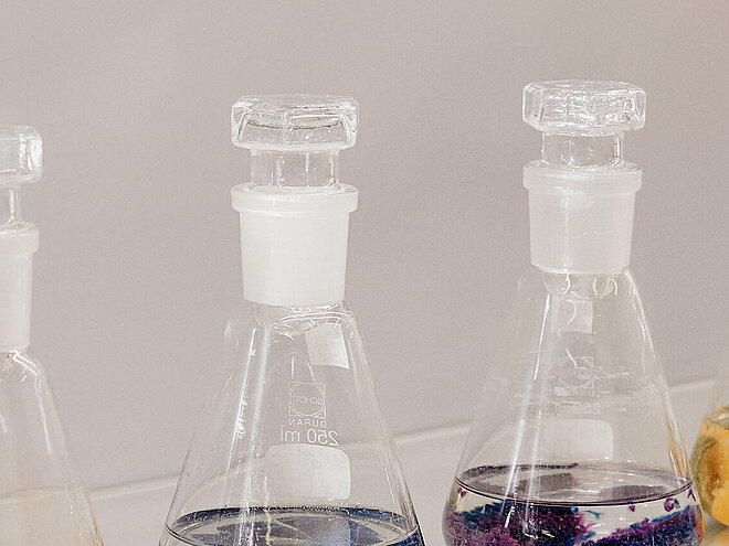 Glass laboratory flasks containing coloured textile pieces