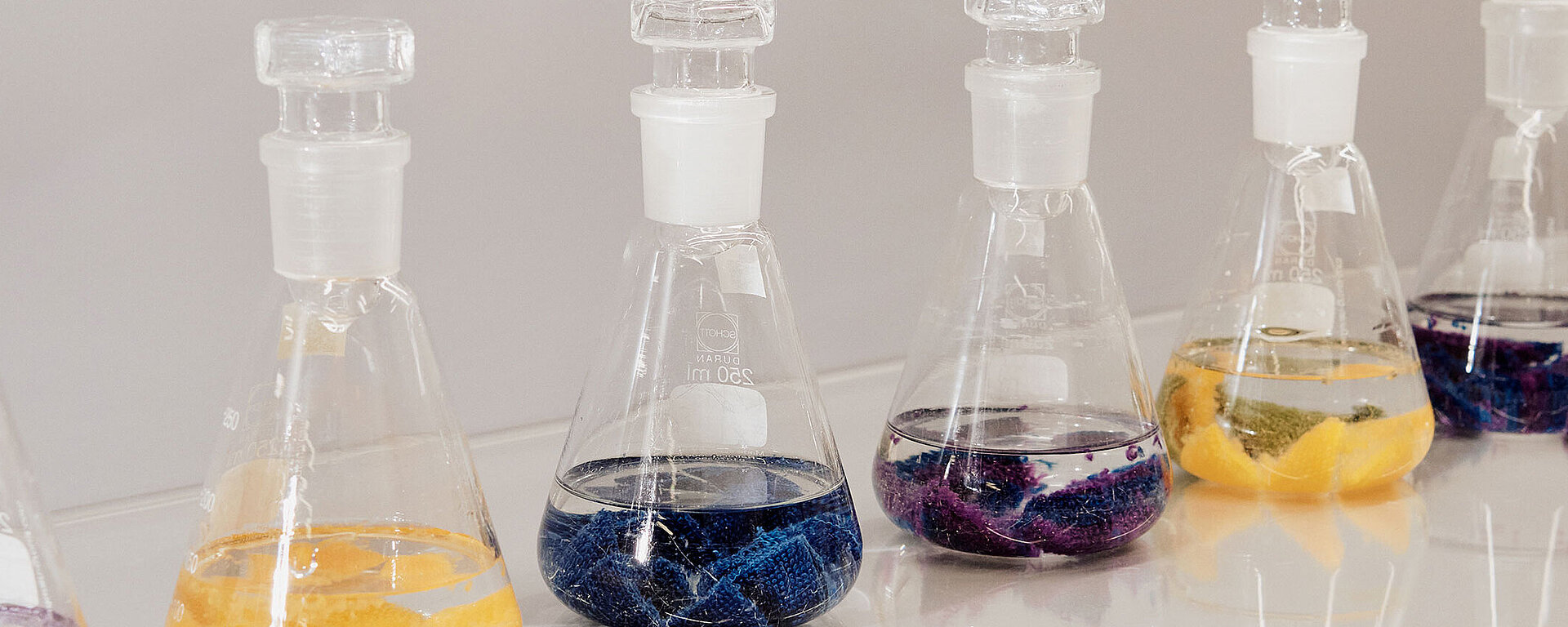 Glaslaborkolben mit farbigen Textilstücken