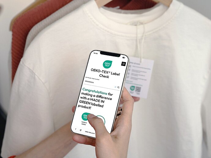 Hand holding a smartphone displaying certification status in the OEKO-TEX Label Check